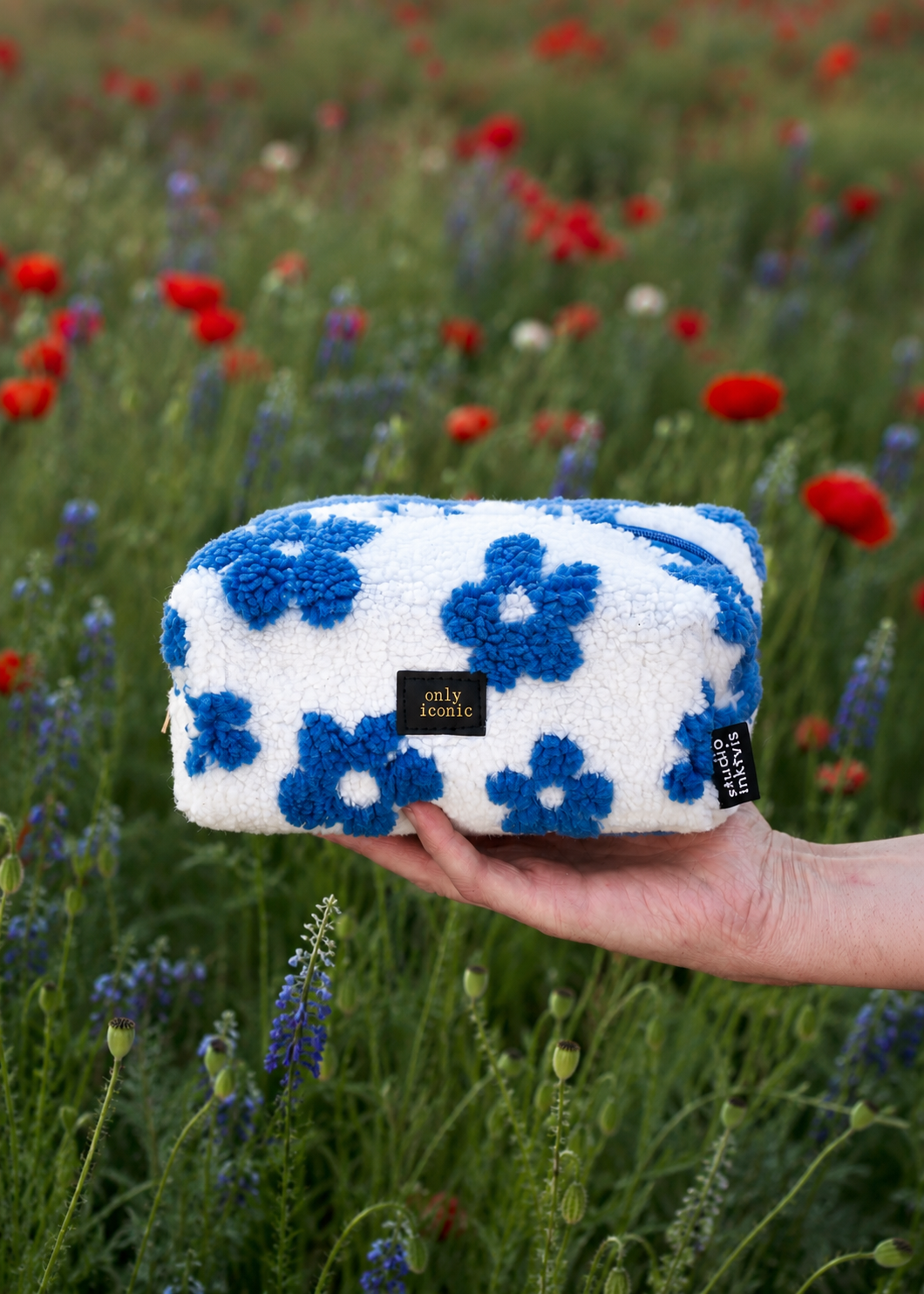 Wit-blauw teddy tasje met bloemenpatroon en Only Iconic label, vastgehouden in een bloemenveld.