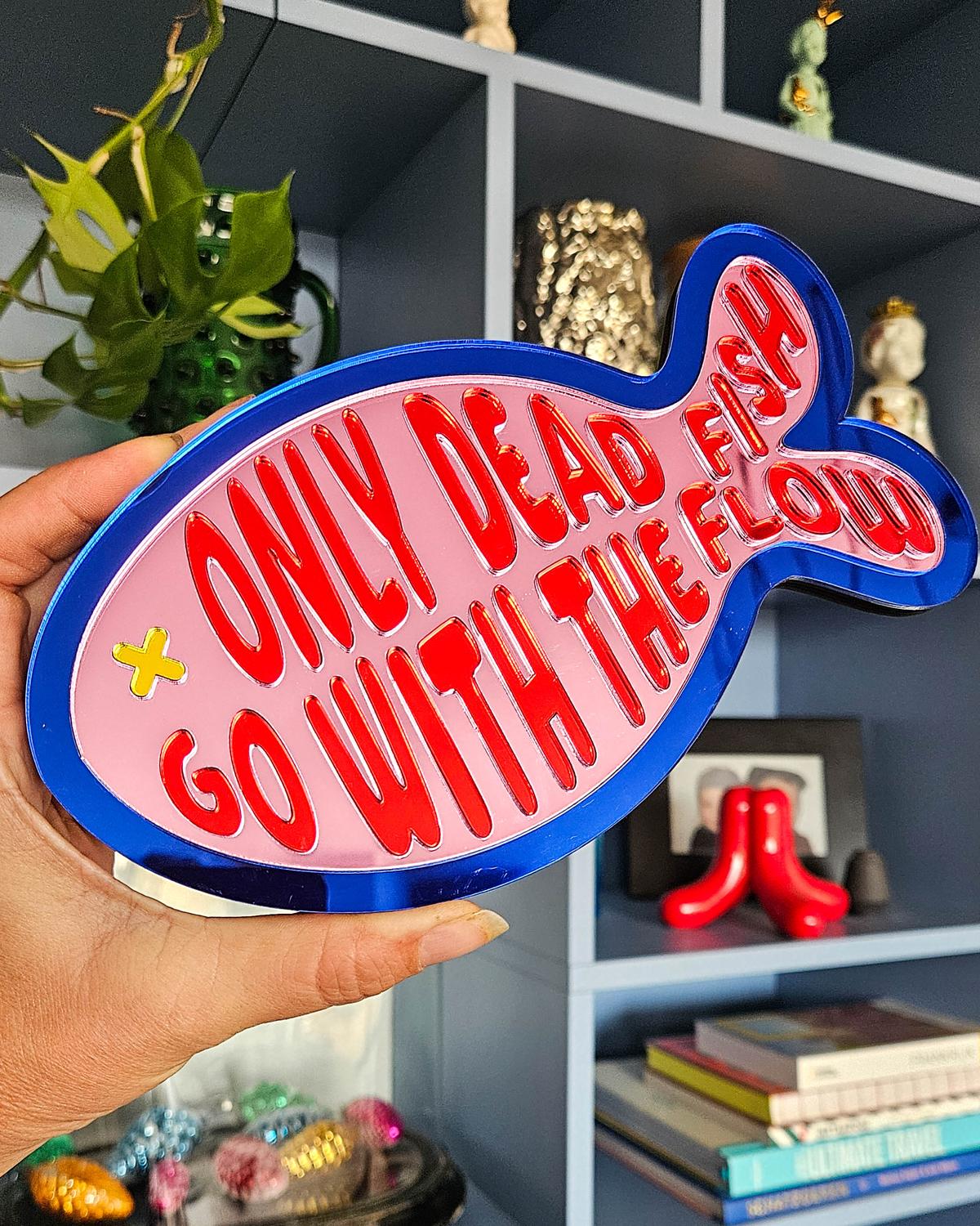 Roze spiegel acrylaat vis wanddecoratie met "Only dead fish go with the flow" tekst en blauwe rand.