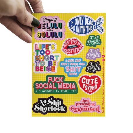 Hand houdt geel A6 stickervel met kleurrijke quotes zoals "Delulu is the Solulu" en "Cute but Psycho".