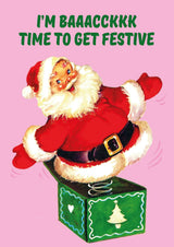 Vintage kerstkaart met vrolijke kerstman die uit een groene surprisebox springt, tekst: "I'm Baaacckkk, Time To Get Festive".