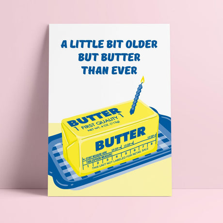 Riso verjaardagskaart met vintage botervloot, gele boter en blauwe kaars, tekst A Little Bit Older But Butter Than Ever.
