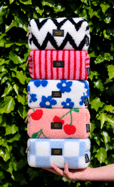 Stapel van vijf zachte teddy etuis in diverse kleuren en prints, waaronder roze met kersen, tegen een groene achtergrond.