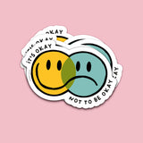 Vaatwasbestendige sticker met overlappende gele blije en blauwe verdrietige smiley en de tekst It's Okay Not To Be Okay.