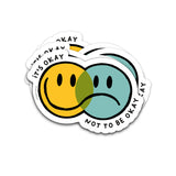 Vaatwasbestendige sticker met overlappende gele blije en blauwe verdrietige smiley en de tekst It's Okay Not To Be Okay.