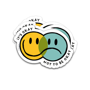 Vaatwasbestendige sticker met overlappende gele blije en blauwe verdrietige smiley en de tekst It's Okay Not To Be Okay.