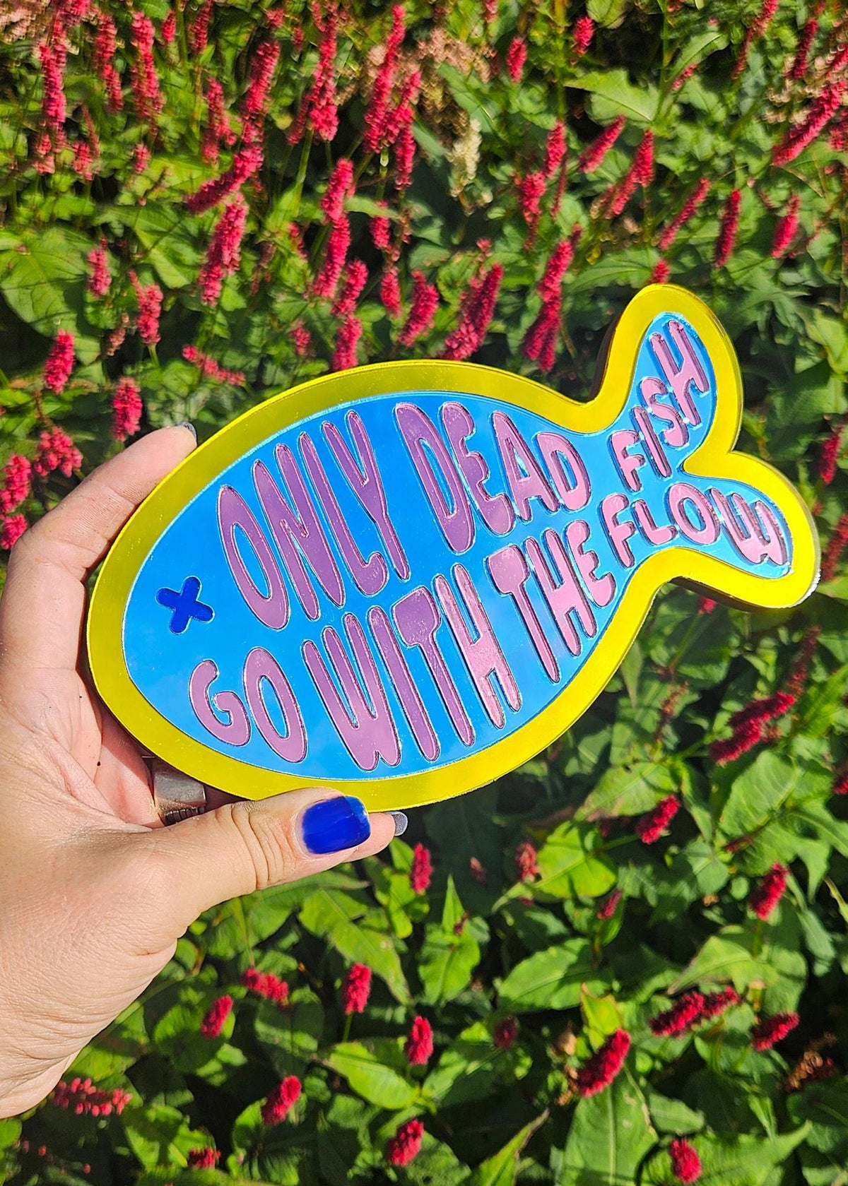 Visvormige wandspiegel van acryl met roze tekst Only dead fish go with the flow, geel en blauw design, 20x11,6 cm.