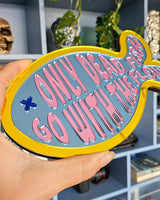Kleurrijke visvormige spiegel van acryl met "Only dead fish go with the flow" tekst in roze op blauw, gele rand.