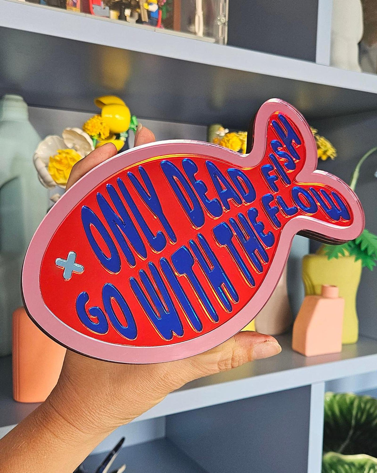 Rood-roze spiegel acrylaat vis wanddecoratie met blauwe tekst "Only dead fish go with the flow".