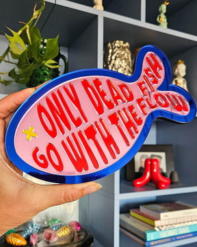 Roze spiegel acrylaat vis wanddecoratie met "Only dead fish go with the flow" tekst en blauwe rand.