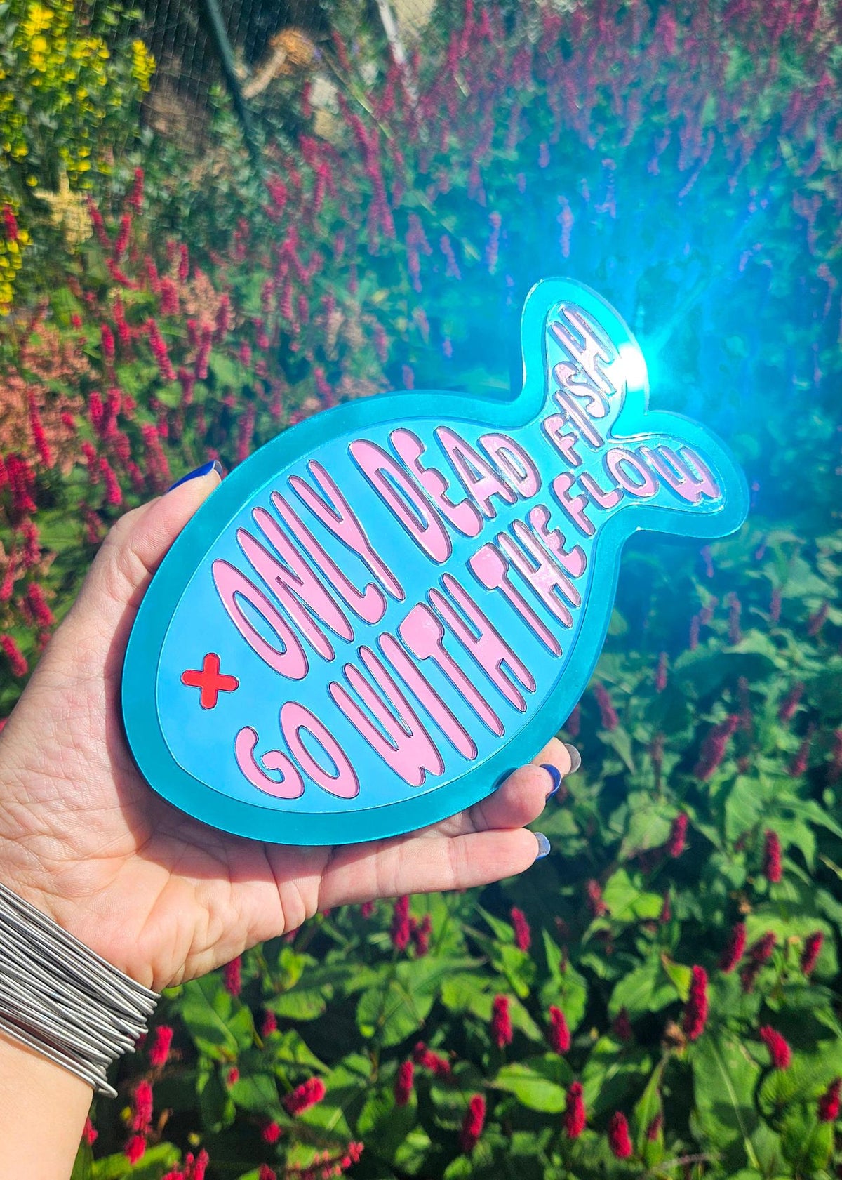 Visvormige spiegel van 20 cm in teal acryl met roze tekst Only dead fish go with the flow en een rood oogje.